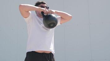 gli sport e tempo libero. forte caucasico uomo Lavorando su utilizzando kettlebell nel il parco, bianca parete sfondo video