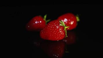 Three beautiful juicy strawberries lie on a dark table on a black background in the light. video