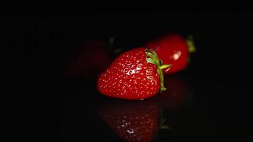 Three beautiful juicy strawberries lie on a dark table on a black background. video