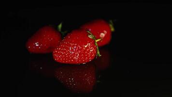 drei schön saftig Erdbeeren Lüge auf ein dunkel Hintergrund. ein fallen von Wasser tropft auf zu das Erdbeere video