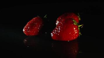 drei saftig frisch Erdbeeren schön Lüge auf ein schwarz Tabelle im ein Strahl von Licht video