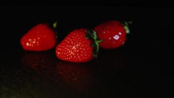 Three fresh strawberries lie on a wet surface in the dark video