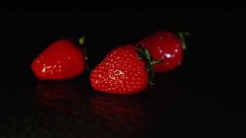 drei frisch Erdbeeren schön Lüge auf ein nass Oberfläche im das dunkel. schwarz Hintergrund video