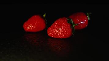 drei frisch Erdbeeren Lüge auf ein nass Oberfläche im das dunkel. schwarz Hintergrund video