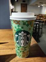 Starbucks Coffee Cup on Wooden Table in Cozy Cafe, Caramel Machiatto Venti Size photo