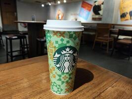 Starbucks Coffee Cup on Wooden Table in Cozy Cafe, Caramel Machiatto Venti Size photo