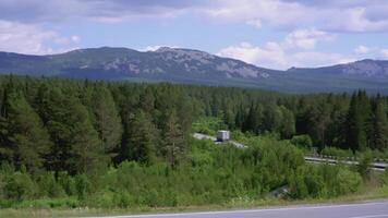 Cars drive along the road in the forest in the mountains. SCENE. The road passes between the trees in the forest. Blue mountains in the background. Warm weather in the forest and mountains video