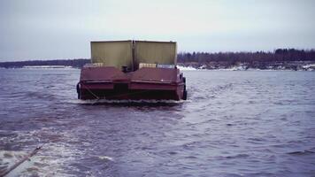 The barge pulls the cargo in the frame. clip. A cargo barge with a trailer floats on the water. A cargo ship is moving along the river. Trees in the background video