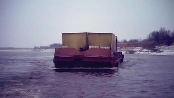 de aak trekt de lading in de kader. klem. een lading aak met een aanhangwagen drijft Aan de water. een lading schip is in beweging langs de rivier. bomen in de achtergrond video