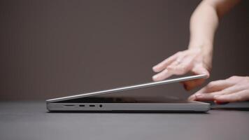 The hand opens the laptop. ACTION. A man opens a laptop with one hand on a gray background. A silver laptop sits on a dark table. Hand lifted the top cover of the netbook video