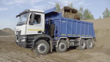 UK, LONDON - MARCH 21, 2022. The excavator pours the earth into the truck. SCENE. Sand from a yellow excavator is poured into a blue KAMAZ. In a quarry, sand is collected in trucks video