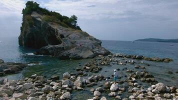 Rock and stone coast with walking tourists. Creative. Beautiful rock on coast in sea. Rock with stones in water near shore with tourists on sunny day video
