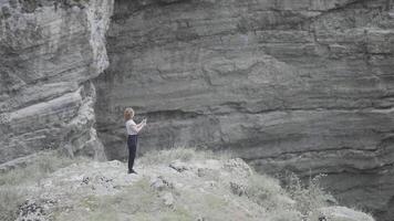 kvinna tar bilder på telefon med steadicam av berg. handling. skön kvinna i de bergen bland stenar tar bilder på telefon. kvinna professionellt skjuter sten landskap och vattenfall på video