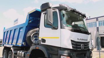 RUSSIA, MOSCOW - MARCH 21, 2022. A large white and blue KAMAZ stands still. SCENE. There is a building and people walking in the background. Kamaz blinking lights on the street. During the day there video