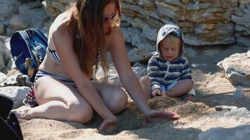 The beach is near the mountains. Creative . A bright seascape where mothers play with their children, build sand towers and approach the shore. video