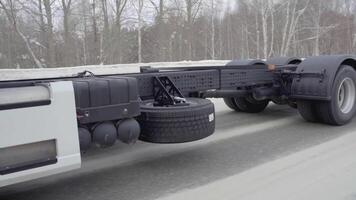 A huge white truck is driving along the road. SCENE. Black wheels Kamaz close-up. White truck rides on the road in winter. A lot of truck wheels are shown in the frame video