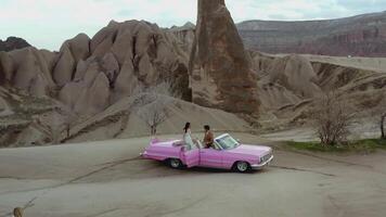 Aerial shot of a couple on a pink vintage car. ACTION. Wedding shooting of a man and a woman in a warm country in the desert. Happy couple on a walk video