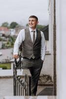 A man in a suit and vest stands on a balcony, smiling photo