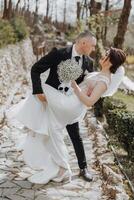 a man in a business suit and a woman in a white dress in nature. The groom hugs and kisses the bride photo