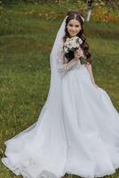 a beautiful bride in a white dress with a bouquet of flowers in her hand walks on the green grass in the garden. Portrait of the bride in the spring garden photo