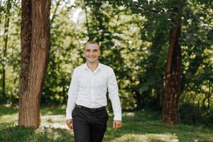 A man in a white shirt and black pants walks through a forest photo