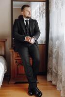 A man in a suit and tie sits on a dresser in front of a mirror photo