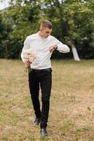 A man wearing a white shirt and black pants is holding a bouquet of flowers photo