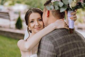 A bride and groom are hugging each other with a bouquet in the groom's hand photo