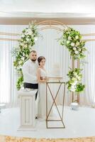 A bride and groom stand in front of a cake on a table photo