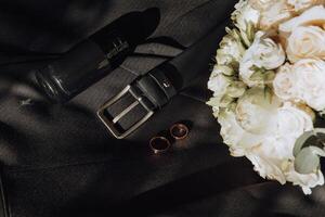 A black belt and a bottle of nail polish sit on a table next to a bouquet of whi photo