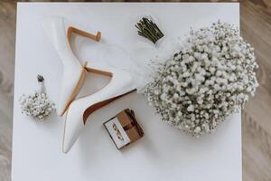 A pair of white shoes and a bouquet of white flowers sit on a table photo