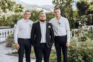 Three men in suits pose for a photo in front of a garden