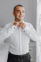 A man in a white shirt is getting dressed and smiling photo