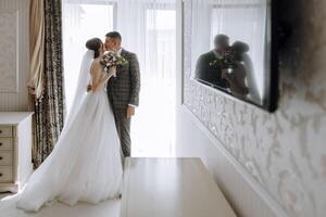 A bride and groom are kissing in front of a mirror photo