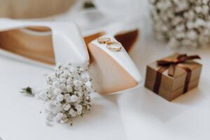 un par de blanco Zapatos con oro anillos en ellos son en un mesa siguiente a un caja con anillos foto