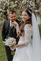 The groom kisses the hand of his bride against the background of a blooming tree in a green garden in spring photo