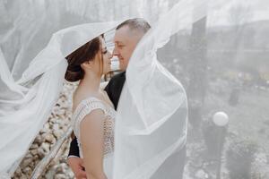 the bride and groom pose under a veil in nature photo