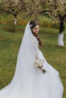 a beautiful bride in a white dress with a bouquet of flowers in her hand walks on the green grass in the garden photo