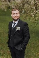 The groom dressed in a black suit walks forward on green grass in nature. An elegant man in a classic black suit. Portrait of a man photo