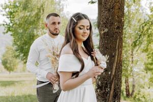 A man and a woman are standing in a field with a tree behind them photo