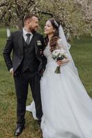 The groom dressed in a black suit embraces his bride in a white dress. Wedding in the spring. Beautiful couple in nature photo