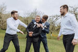 four boys dressed in suits and white shirts, having fun in nature. The groom and his friends are celebrating a special event photo