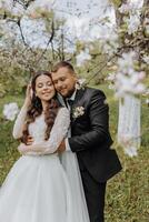 the first meeting of the bride and groom in a blooming garden. The bride in an incredible white dress with expensive hair and makeup. The groom in a black suit goes to the bride photo