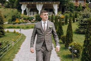 A man in a suit walks down a path in a garden photo