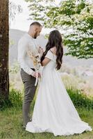 A bride and groom are standing in a field with a tree behind them photo