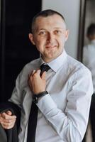 A man in a suit and tie is smiling and adjusting his tie photo