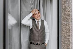 A man in a suit and vest stands in front of a window, smiling photo