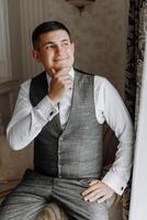 A man in a suit and vest is sitting on a couch and looking out the window photo