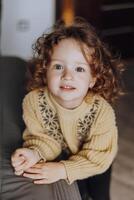 A young girl with curly hair is wearing a yellow sweater and smiling photo