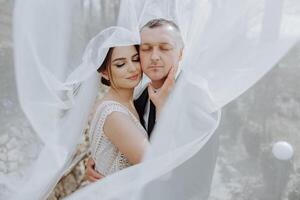 the bride and groom pose under a veil in nature photo